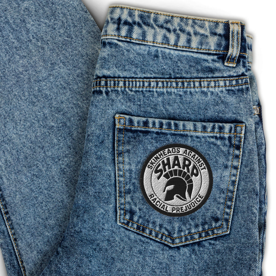 Runder bestickter SHARP-Aufnäher mit Trojan-Helm und Schriftzug „Skinheads Against Racial Prejudice", aufgenäht auf einer Jeans-Gesäßtasche