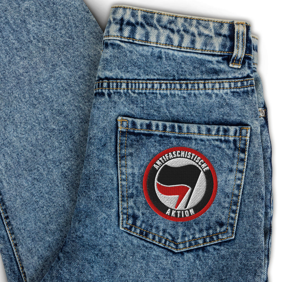 Runder bestickter Aufnäher mit dem Zwei-Fahnen-Symbol der Antifaschistischen Aktion, aufgenäht auf einer Jeans-Gesäßtasche